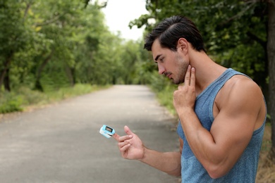 Young man checking pulse with medical device after training in park. Space for text