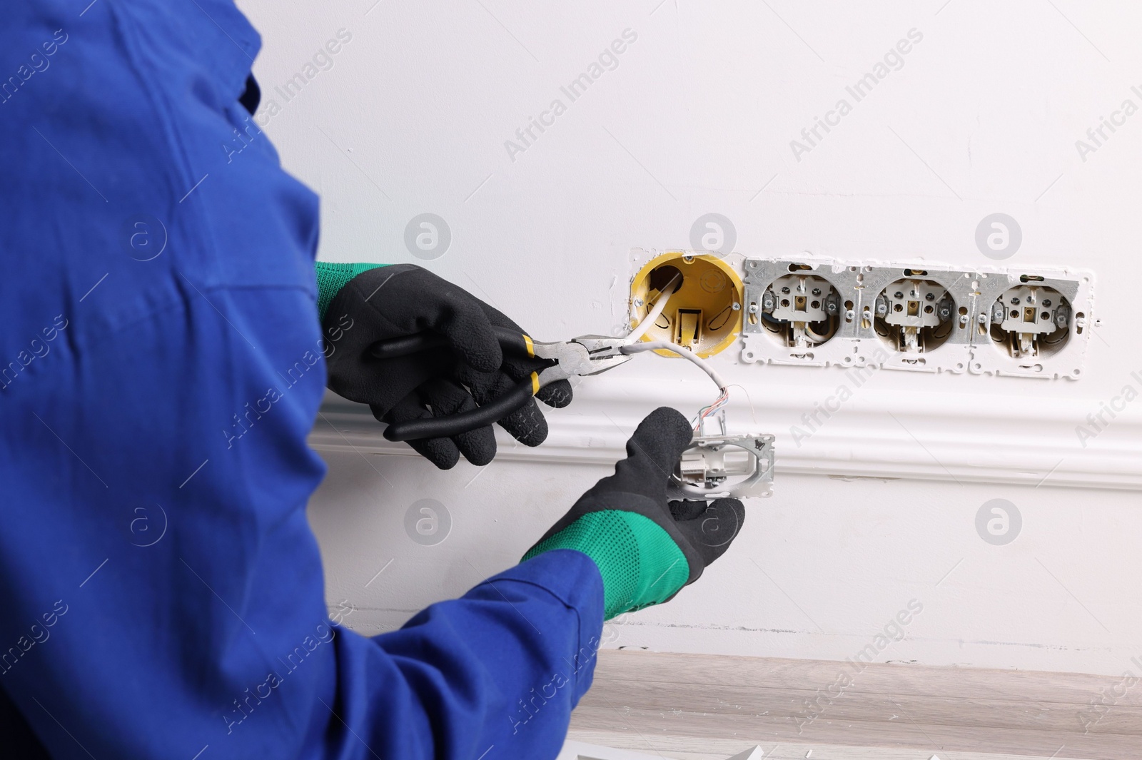 Photo of Professional repairman fixing power sockets with pliers indoors, closeup