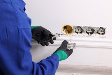 Photo of Professional repairman fixing power sockets with pliers indoors, closeup