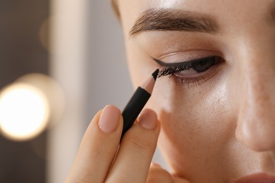 Photo of Makeup product. Woman applying black eyeliner indoors, closeup