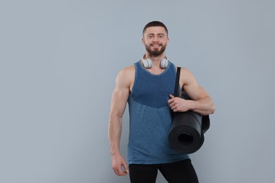 Photo of Handsome man with fitness mat and headphones on grey background, space for text