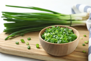 Photo of Wooden bowl with cut green onion on board. Space for text