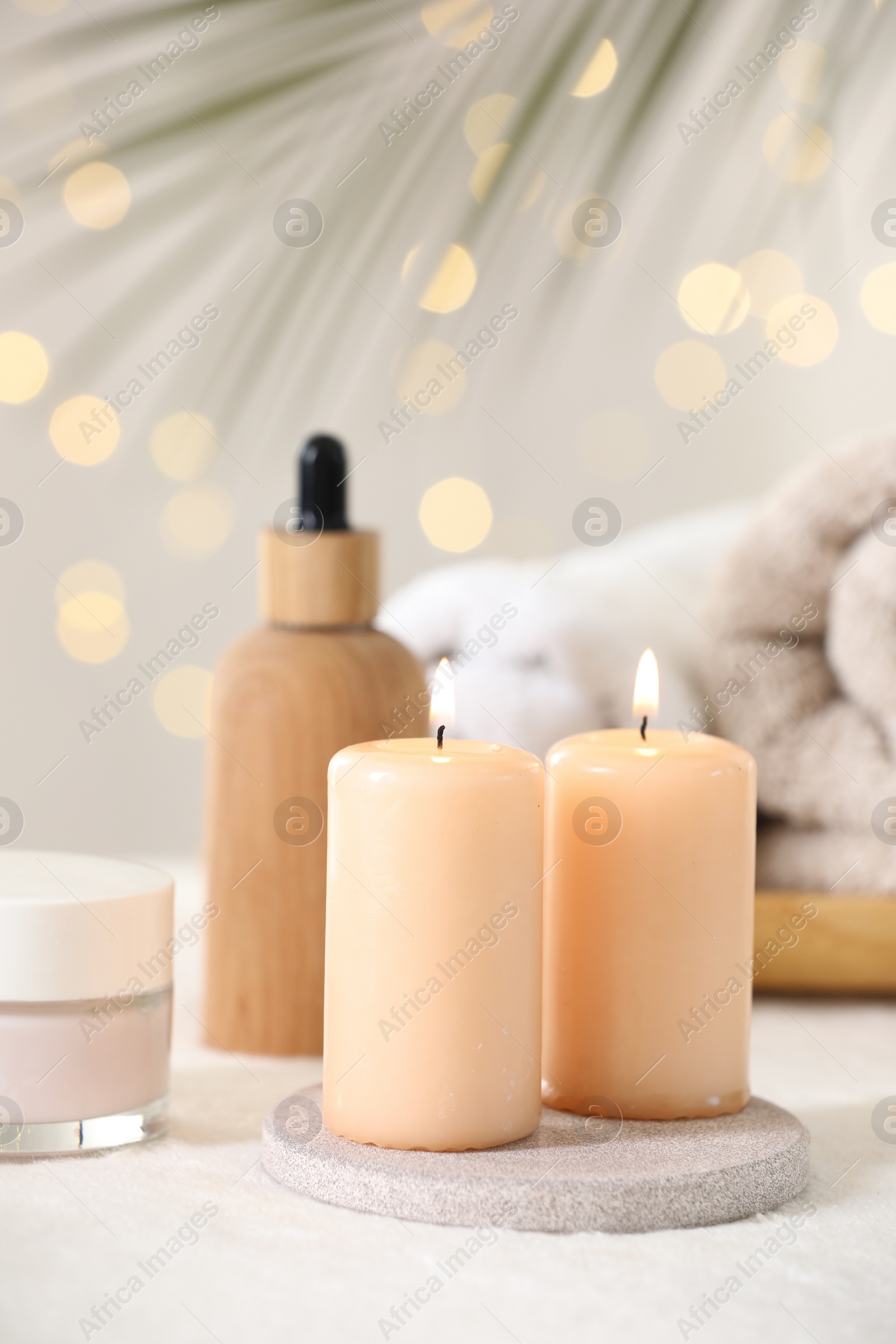 Photo of Spa composition. Burning candles and cosmetic products on soft white surface