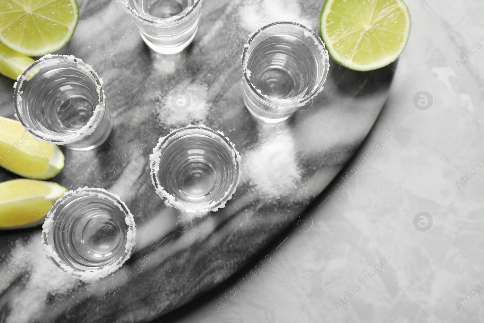 Photo of Mexican Tequila shots, lime slices and salt on grey marble table, top view