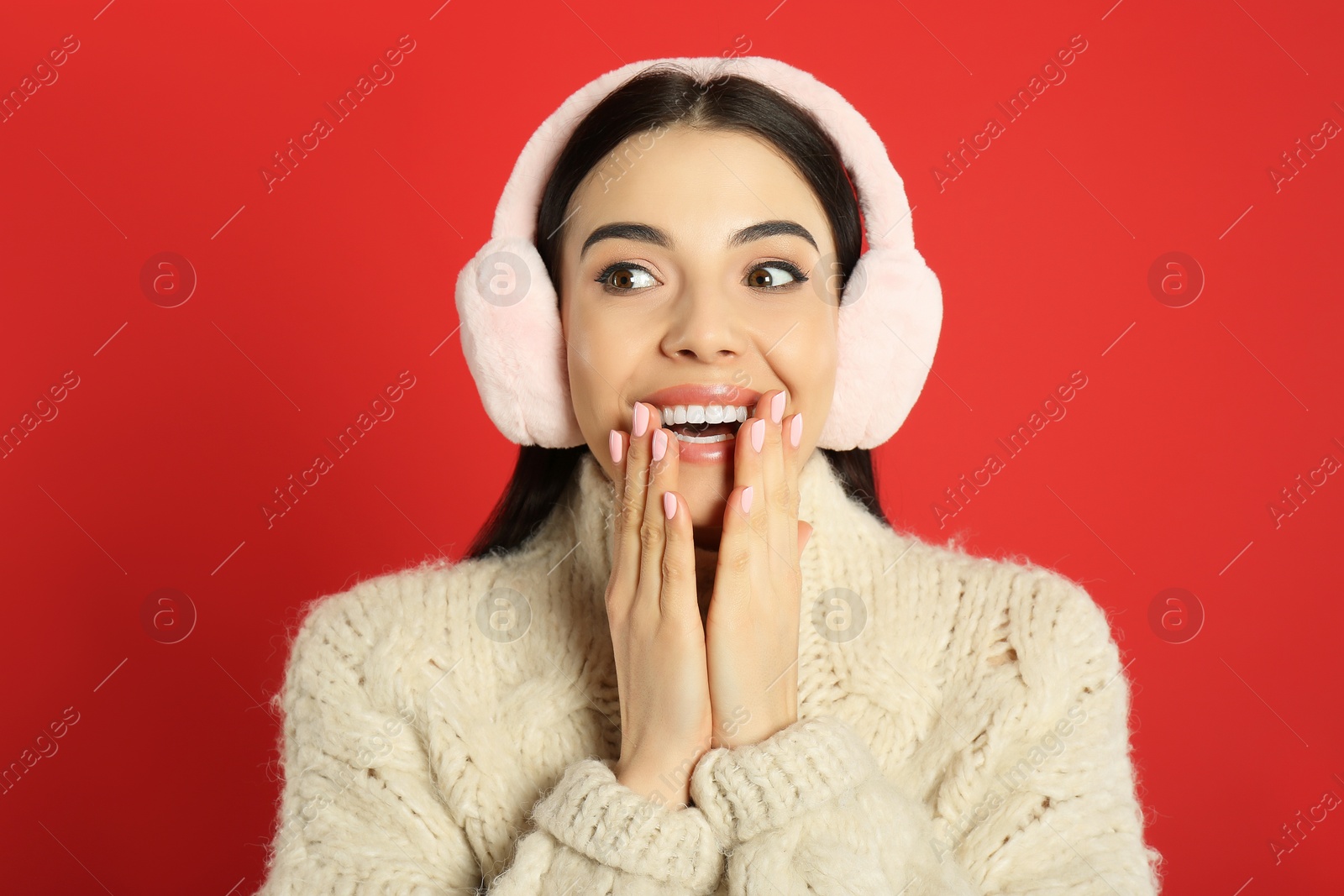 Photo of Beautiful young woman wearing earmuffs on red background