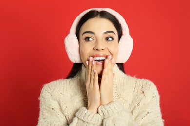 Beautiful young woman wearing earmuffs on red background