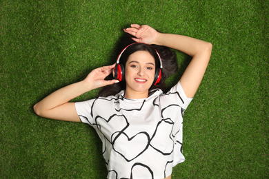 Photo of Young woman listening to audiobook while lying on grass, top view