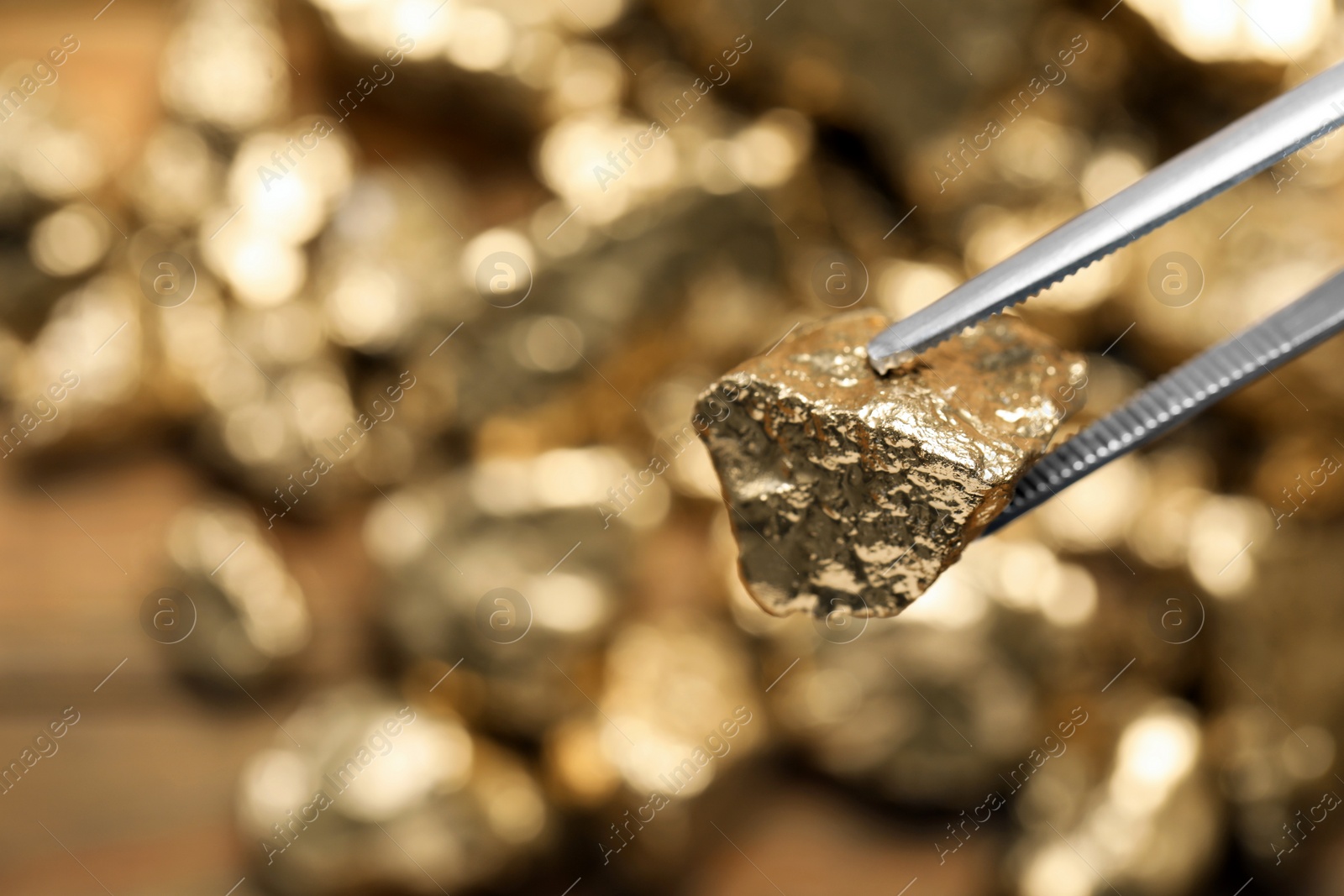 Photo of Tweezers with gold nugget against blurred background, closeup. Space for text