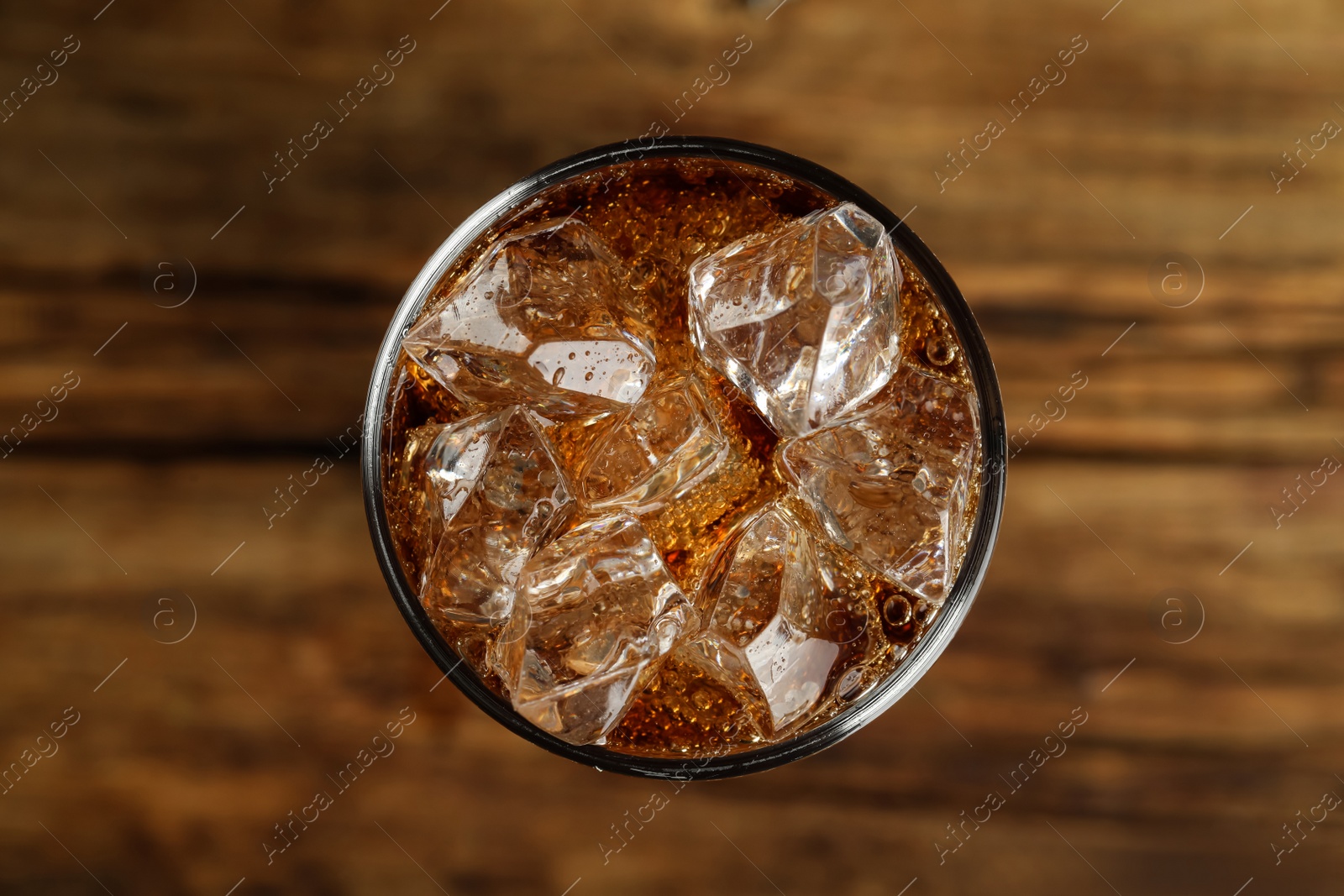 Photo of Glass of refreshing soda water with ice cubes on wooden table, top view