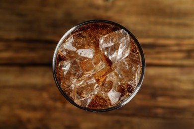 Glass of refreshing soda water with ice cubes on wooden table, top view