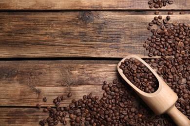 Photo of Scoop with roasted coffee beans on wooden table, flat lay. Space for text