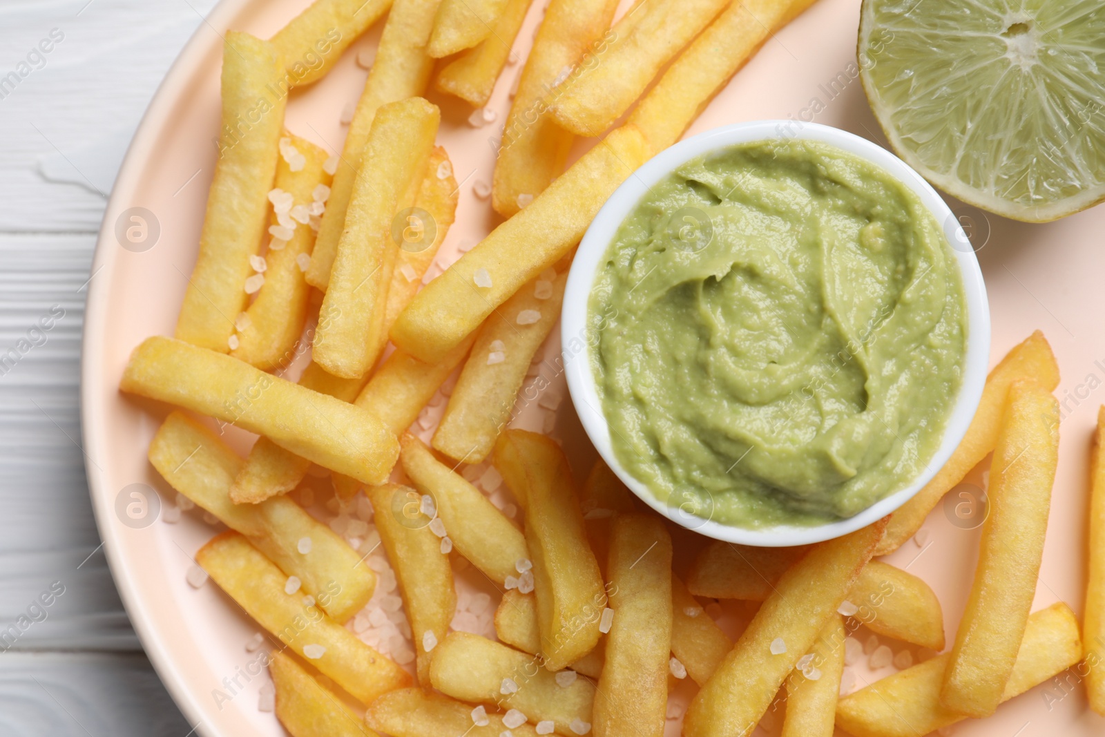 Photo of Plate with french fries, lime and avocado dip on white wooden table, top view