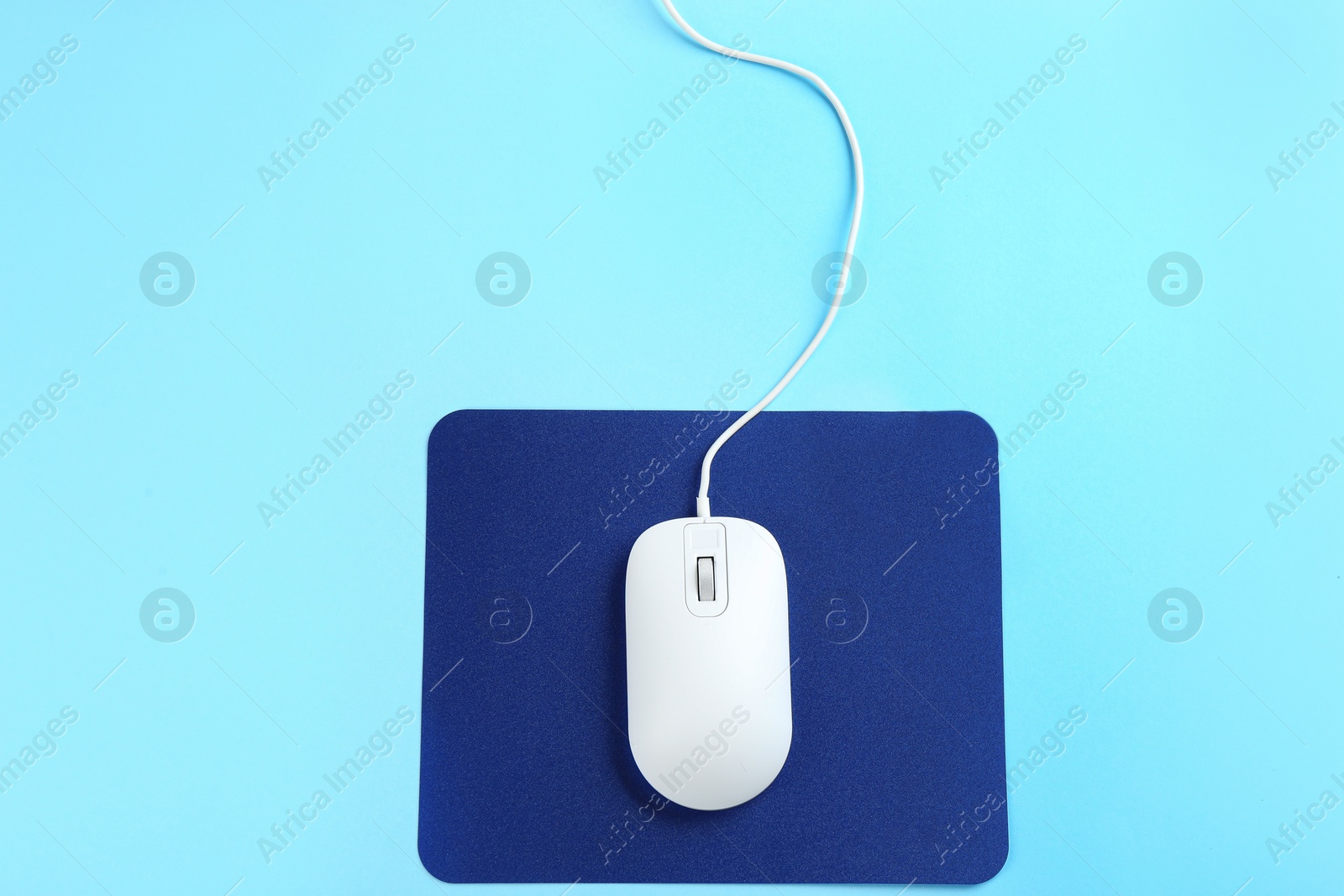 Photo of Modern wired mouse and pad on light blue background, top view