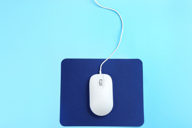 Photo of Modern wired mouse and pad on light blue background, top view