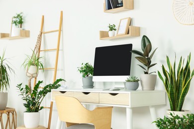 Photo of Comfortable workplace with modern computer and different houseplants in room