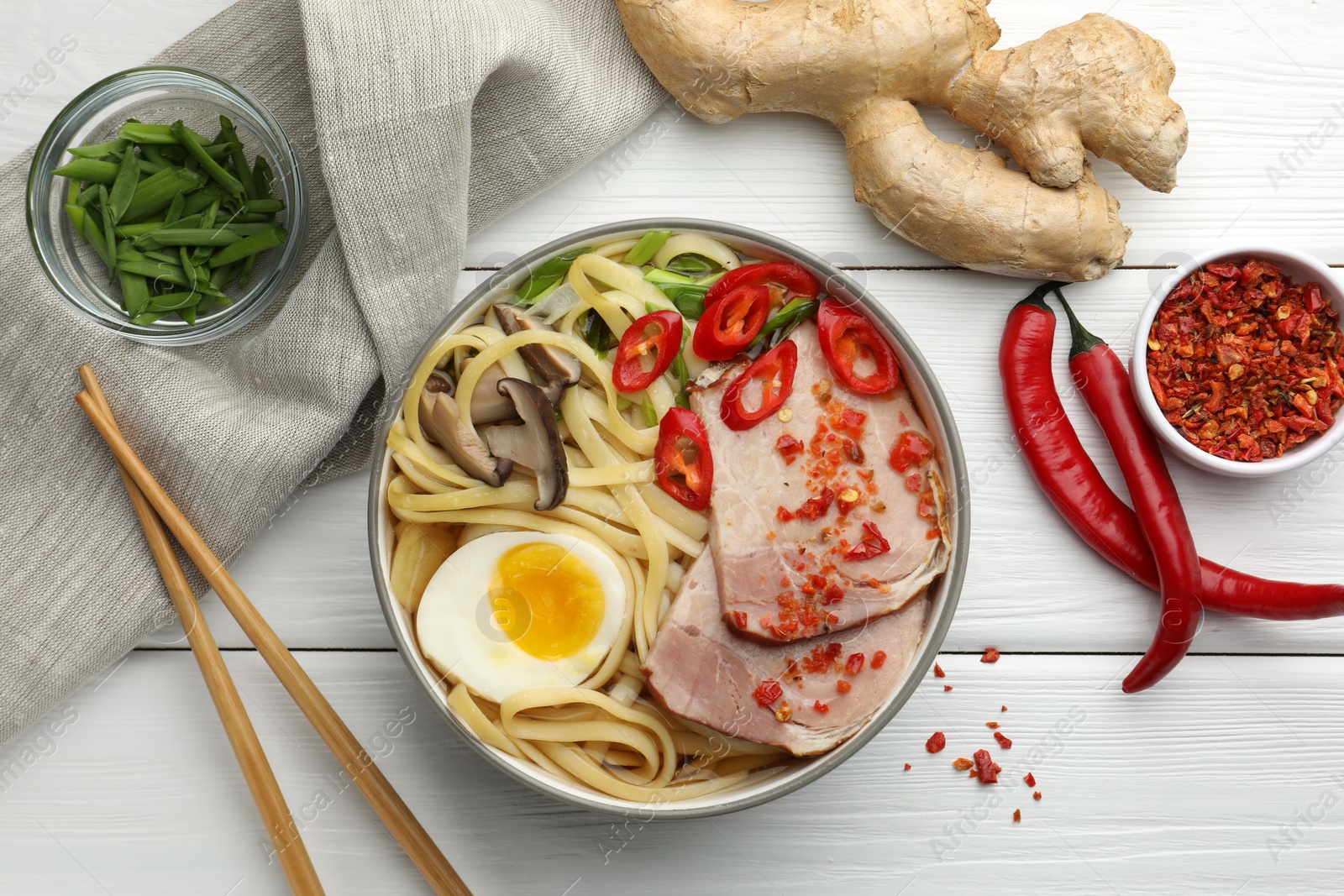 Photo of Delicious ramen in bowl, chopsticks and ingredients on white wooden table, flat lay. Noodle soup