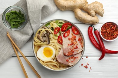 Photo of Delicious ramen in bowl, chopsticks and ingredients on white wooden table, flat lay. Noodle soup