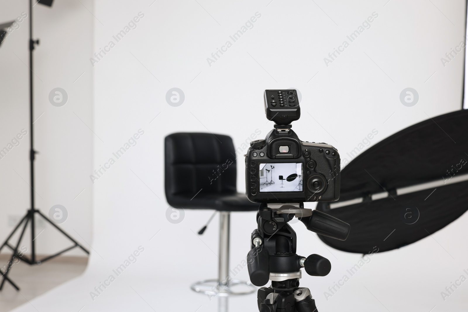 Photo of Camera on tripod, bar stool and professional lighting equipment in modern photo studio, space for text