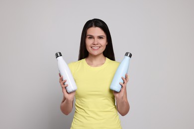 Young woman with thermo bottles on light grey background