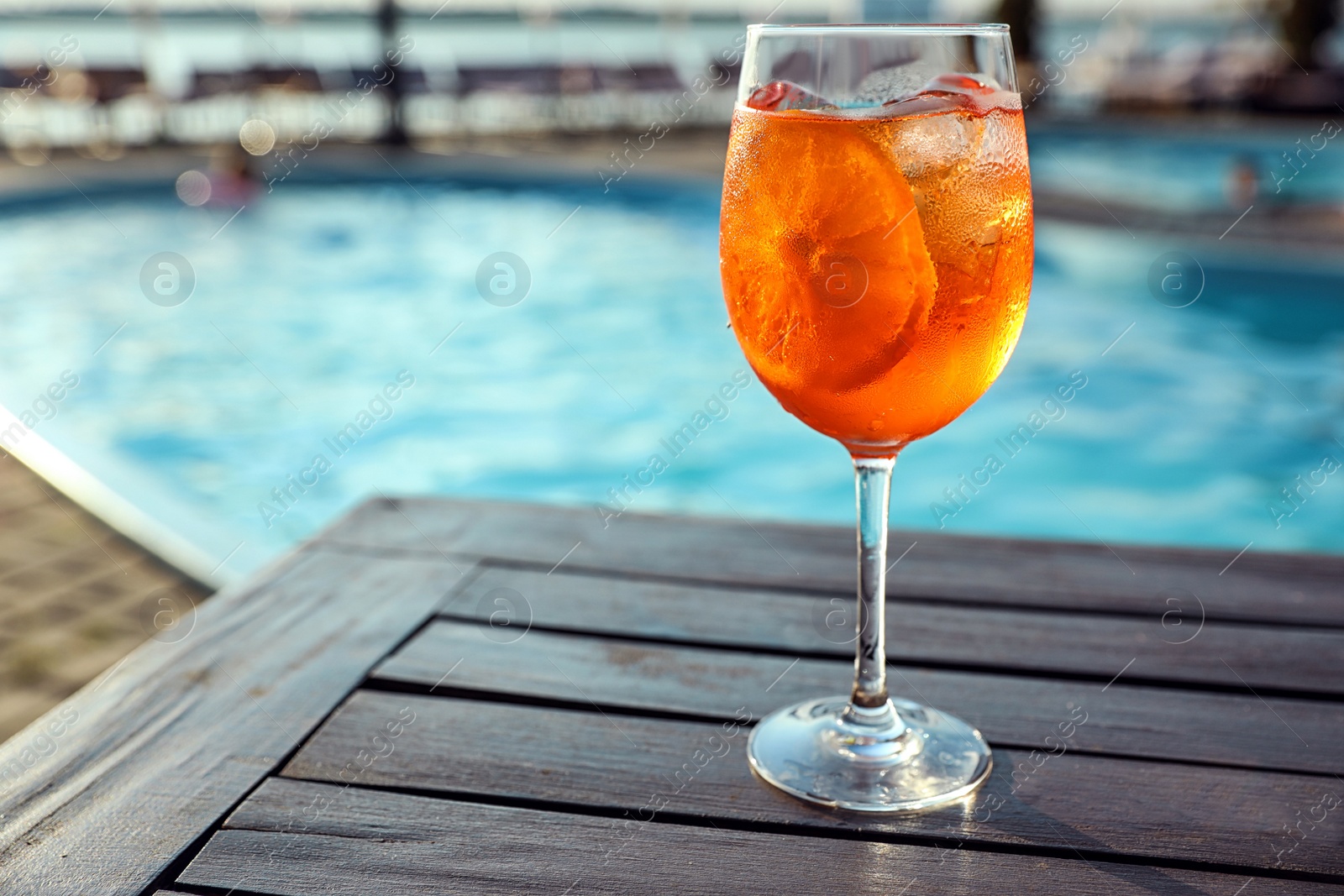 Photo of Glass of fresh summer cocktail on wooden table near swimming pool outdoors. Space for text