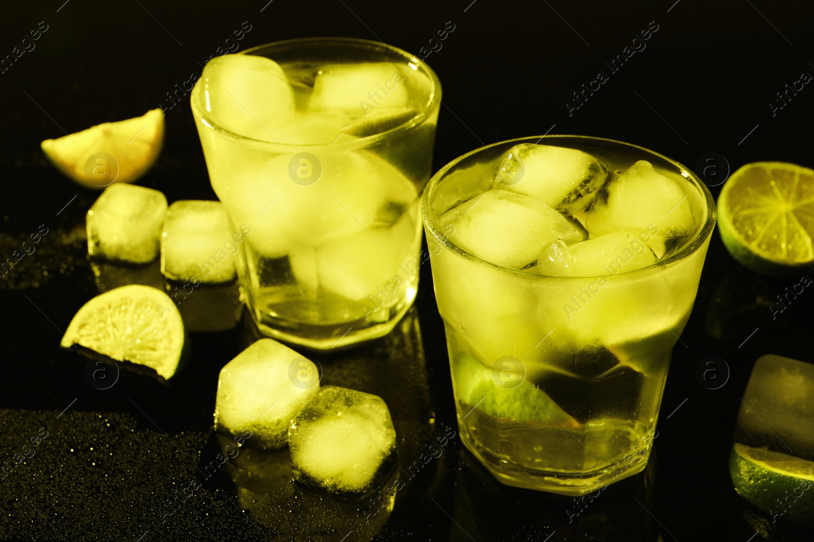 Photo of Shot glasses of vodka with ice cubes and lime slices on dark background