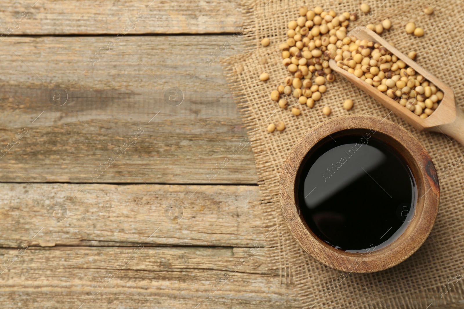 Photo of Soy sauce in bowl and soybeans on wooden table, flat lay. Space for text