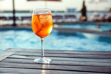 Glass of fresh summer cocktail on wooden table near swimming pool outdoors. Space for text