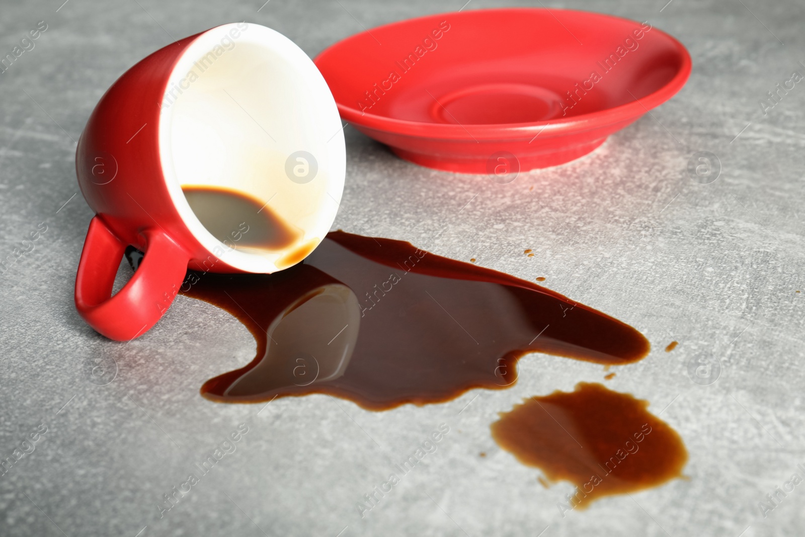 Photo of Cup with saucer and coffee spill on grey table