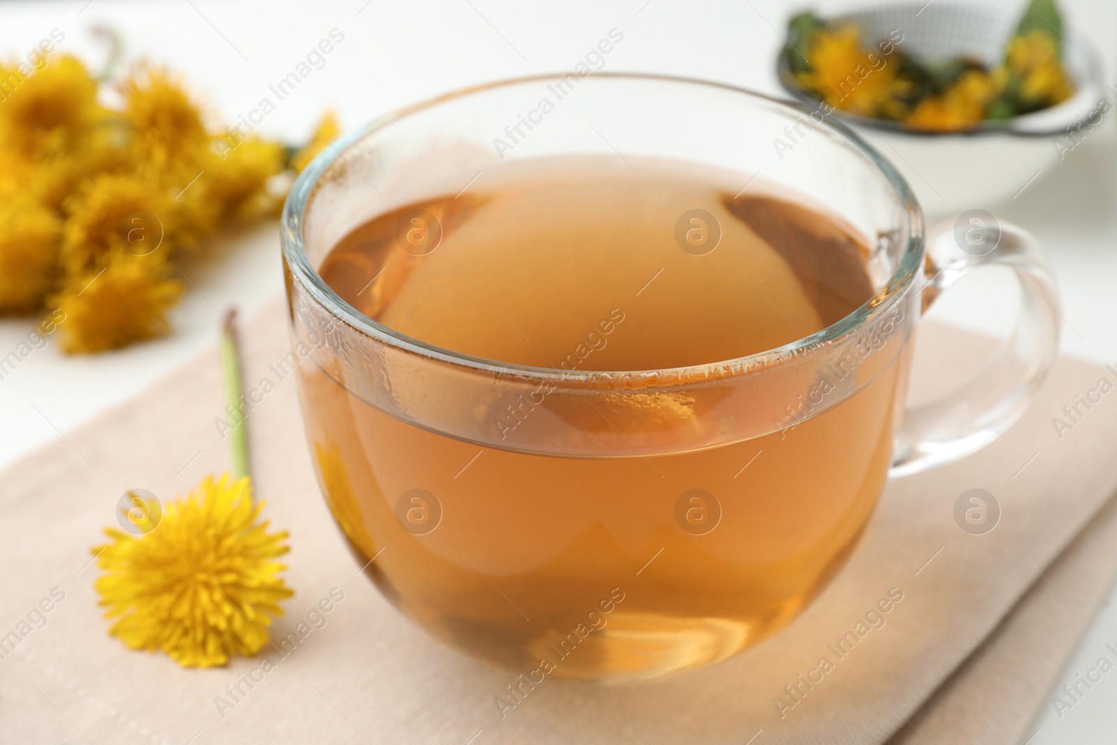 Photo of Delicious fresh tea and dandelion flowers on white table, closeup