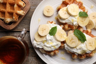 Delicious Belgian waffles with banana and whipped cream served on wooden table, flat lay