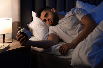 Photo of Frustrated man with alarm clock on bed. Insomnia problem