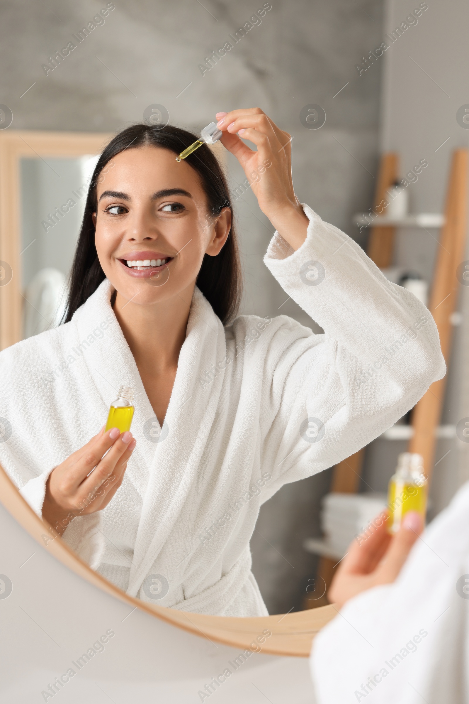 Photo of Beautiful young woman applying serum onto her face in bathroom