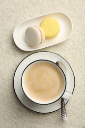 Photo of Tasty cappuccino in cup and macarons on light textured table, flat lay