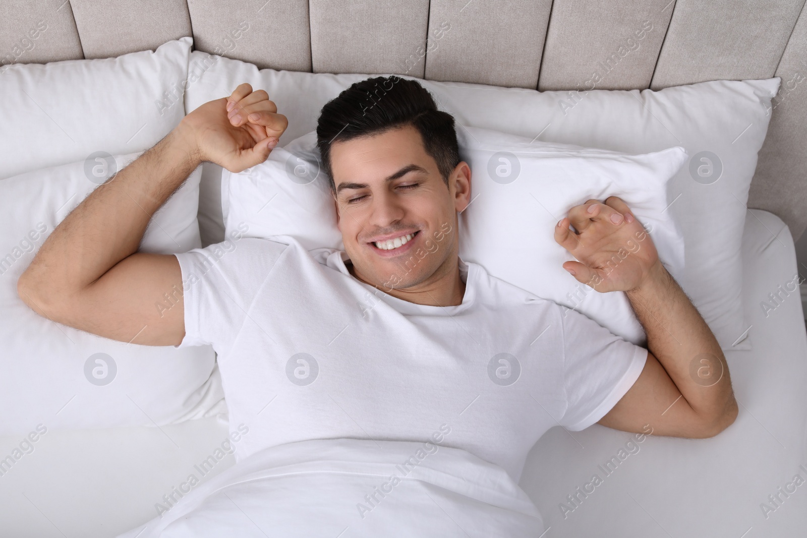 Photo of Happy man awakening in bed at home, top view