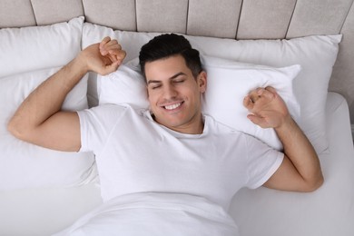 Happy man awakening in bed at home, top view