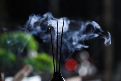 Photo of Incense sticks smoldering in holder on blurred background, closeup