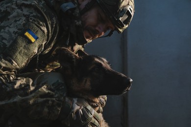 Photo of Ukrainian soldier with German shepherd dog near wall outdoors. Space for text