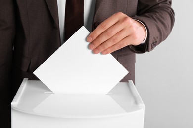 Photo of Man putting his vote into ballot box on light grey background, closeup