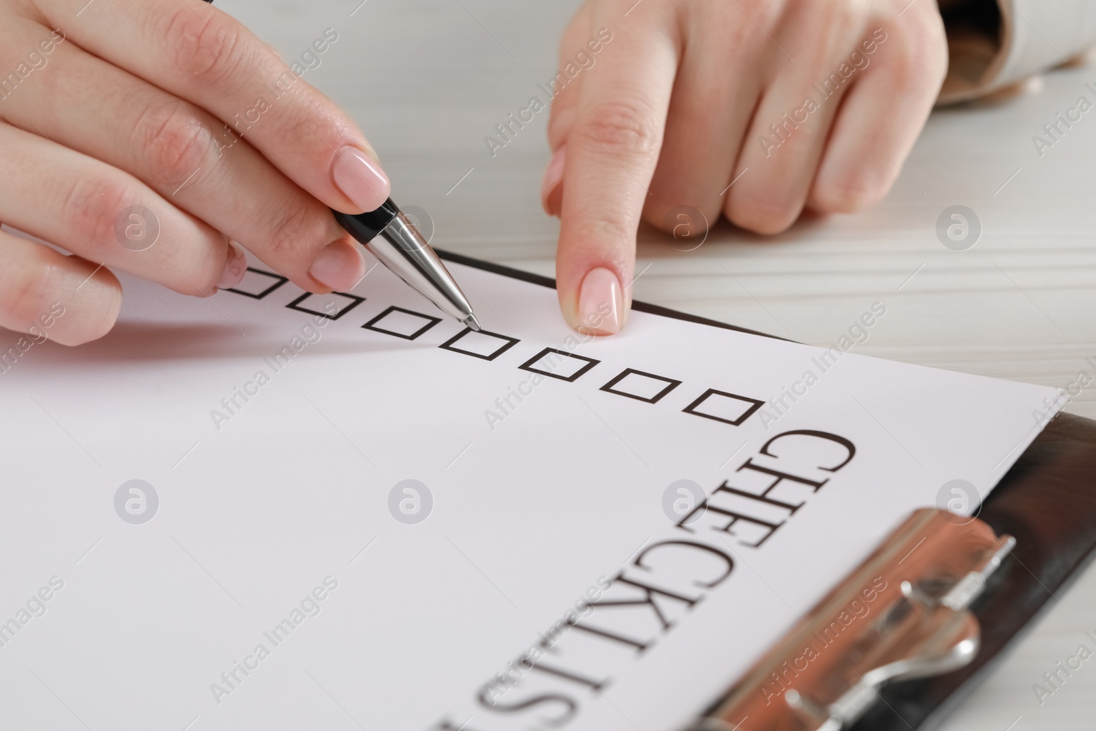 Photo of Woman filling Checklist at white wooden table, closeup