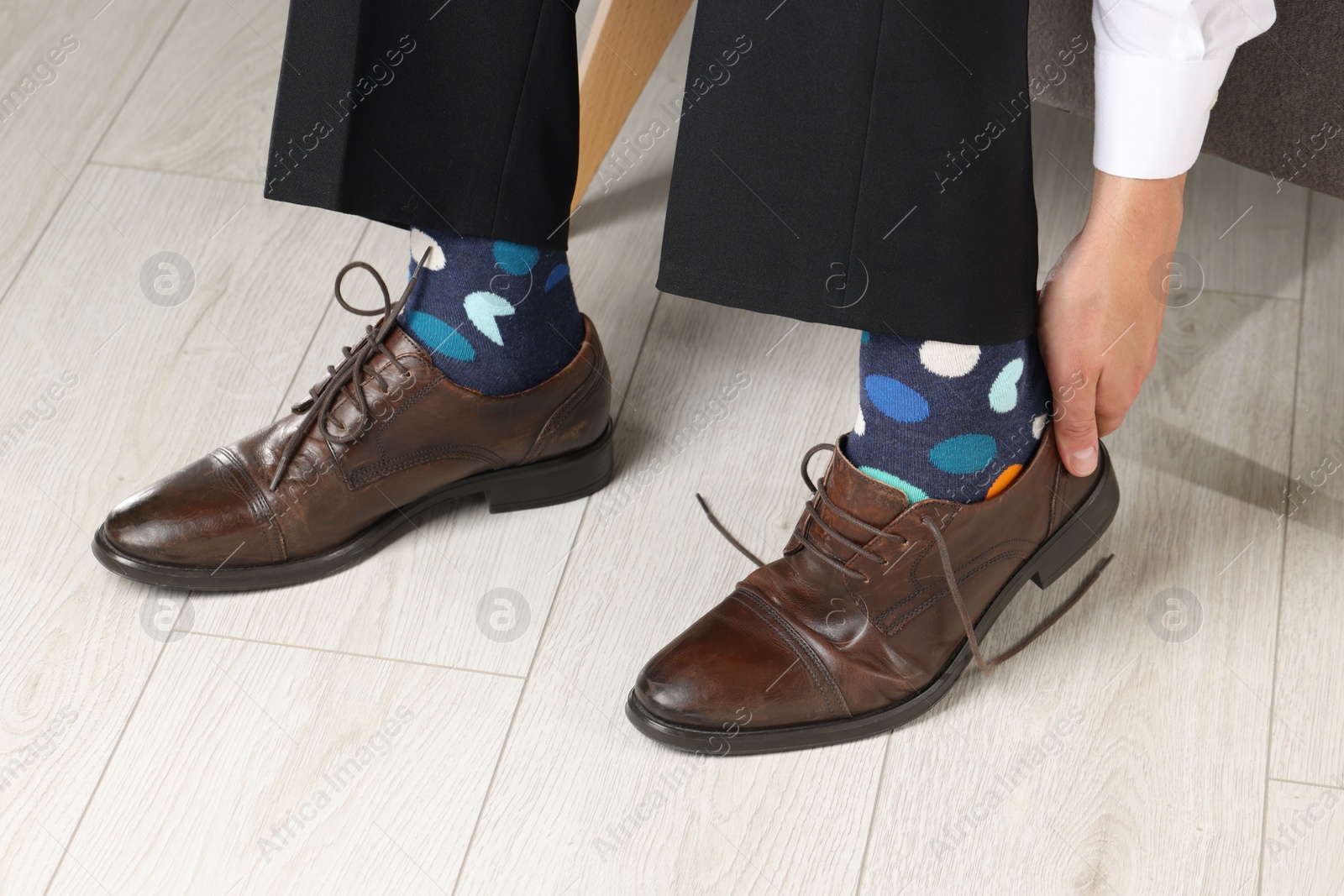 Photo of Man with colorful socks putting on stylish shoes indoors, closeup