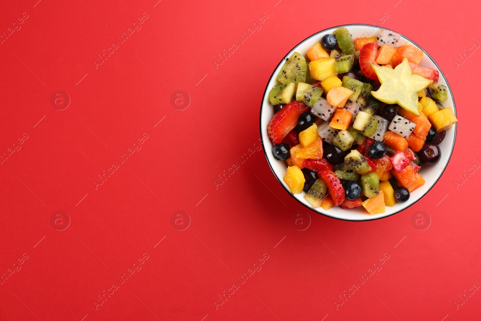 Photo of Delicious exotic fruit salad on red background, top view. Space for text