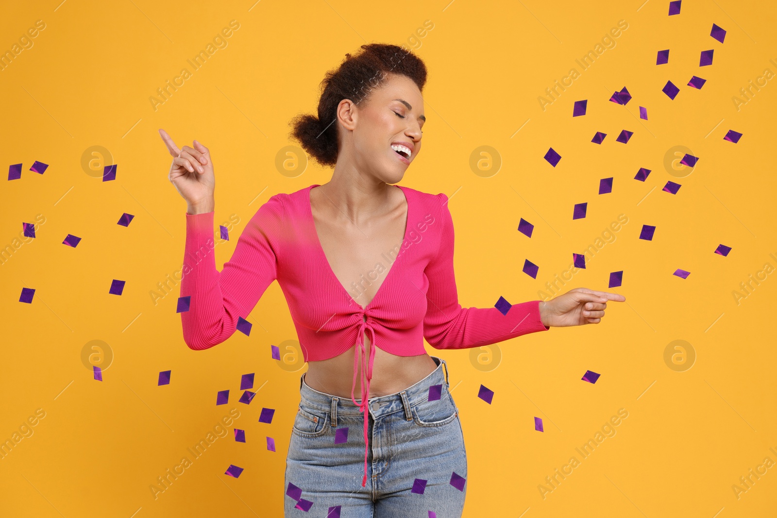 Image of Happy woman dancing under flying confetti on orange background