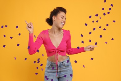 Happy woman dancing under flying confetti on orange background