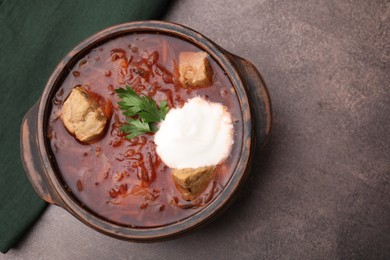 Photo of Tasty borscht with sour cream in bowl on brown textured table, top view. Space for text