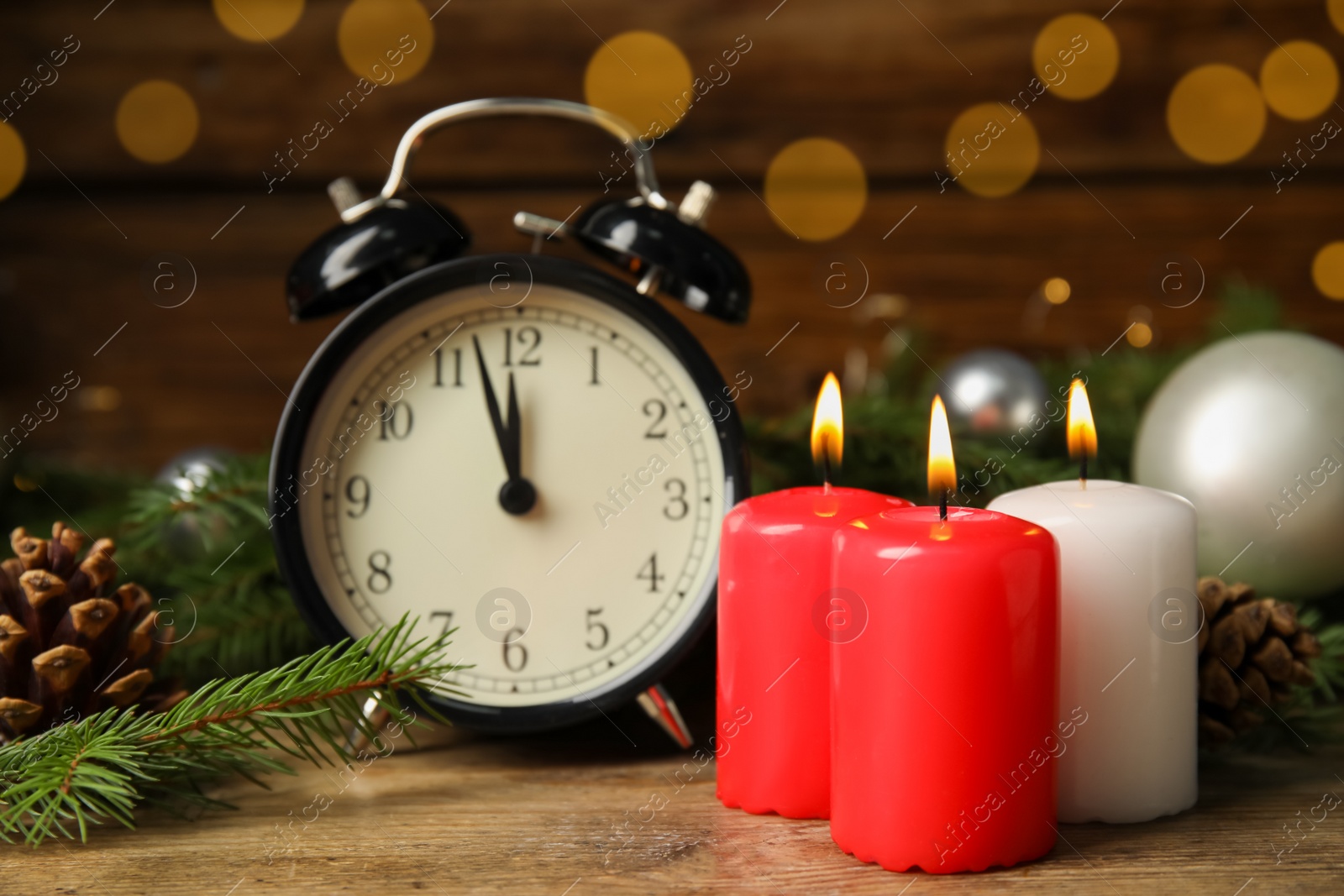 Photo of Alarm clock, burning candles and Christmas decor on wooden table, bokeh effect