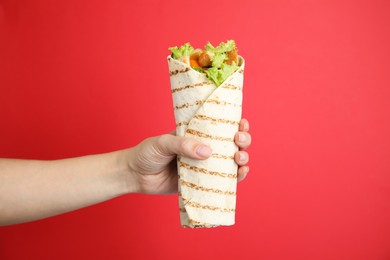 Photo of Woman holding delicious chicken shawarma on red background, closeup
