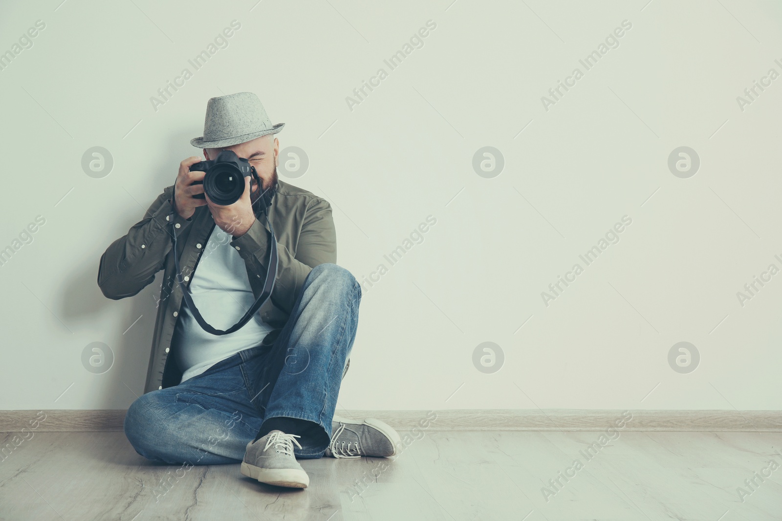 Image of Professional photographer with camera on floor near white wall. Space for text