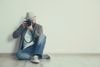 Professional photographer with camera on floor near white wall. Space for text