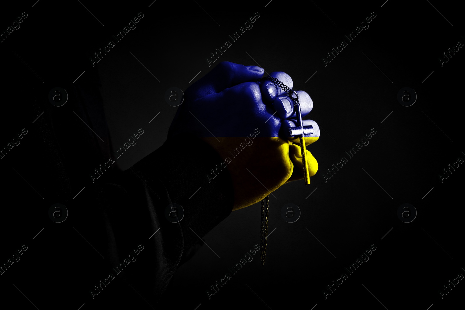 Image of Pray for Ukraine. Priest with cross praying on black background, closeup