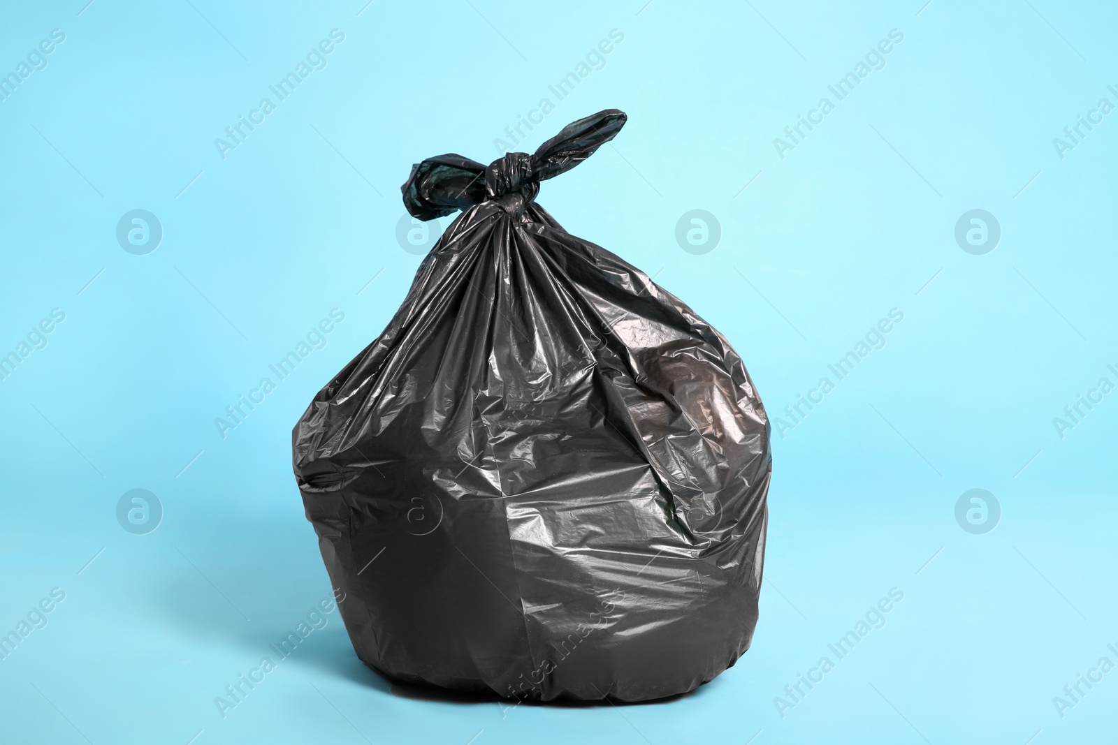 Photo of Black trash bag full of garbage on light blue background